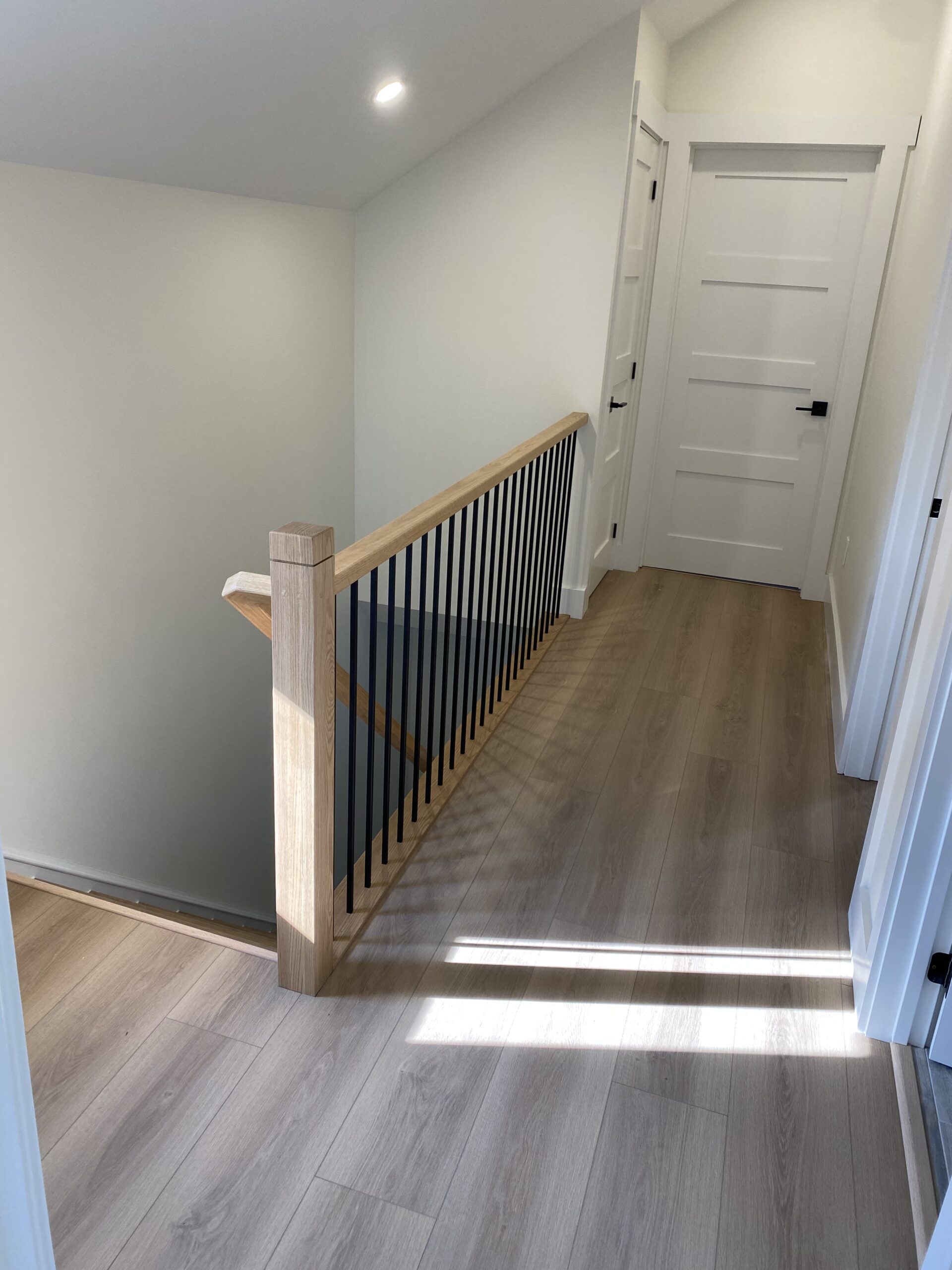 Newly renovated landing with new doors, trim and wood-style flooring, looking towards new hardwood stairs leading to the main level of a Hamilton home.