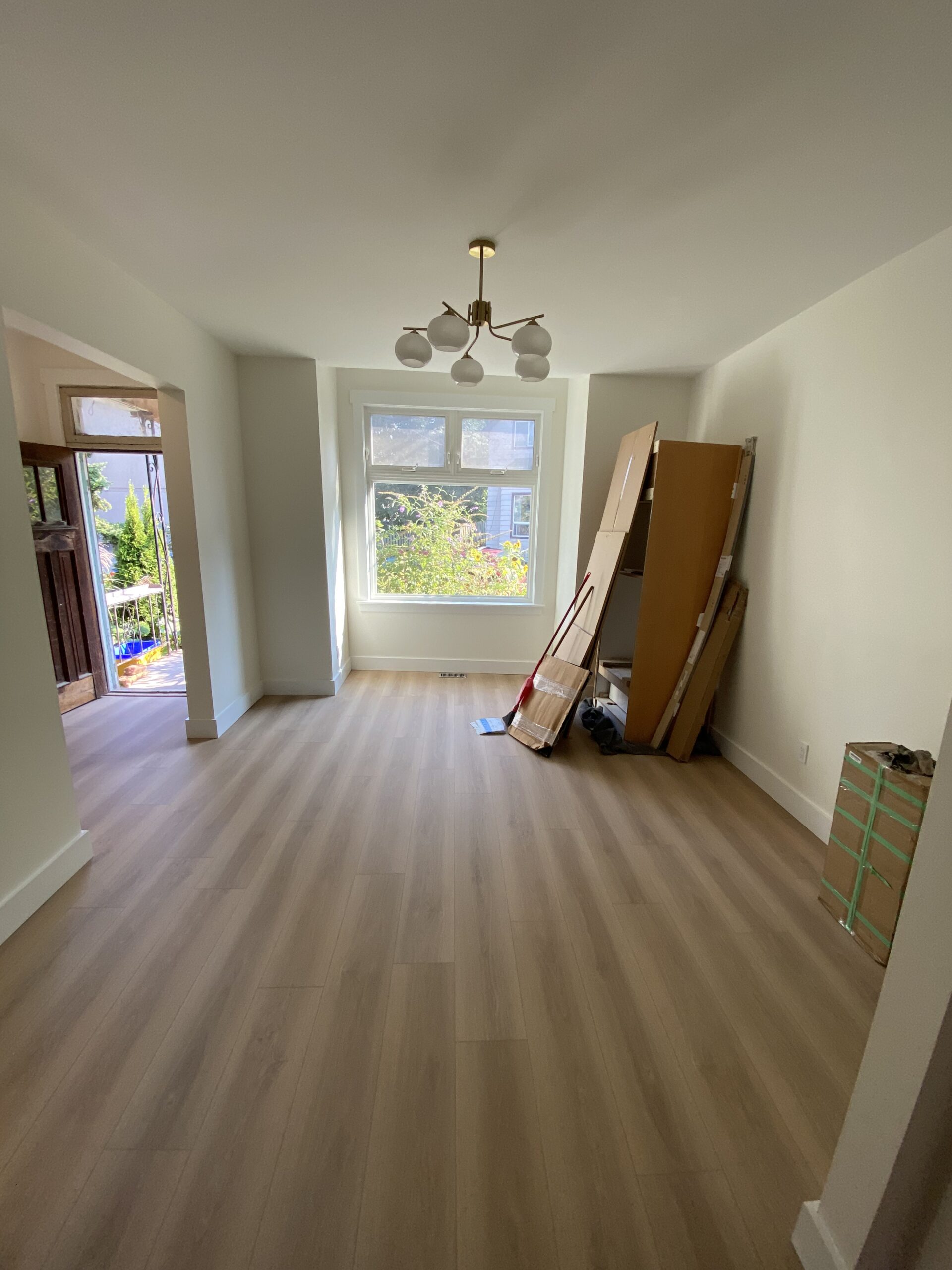 Finished wood-style flooring in an open living room with a large window looking out onto the street.