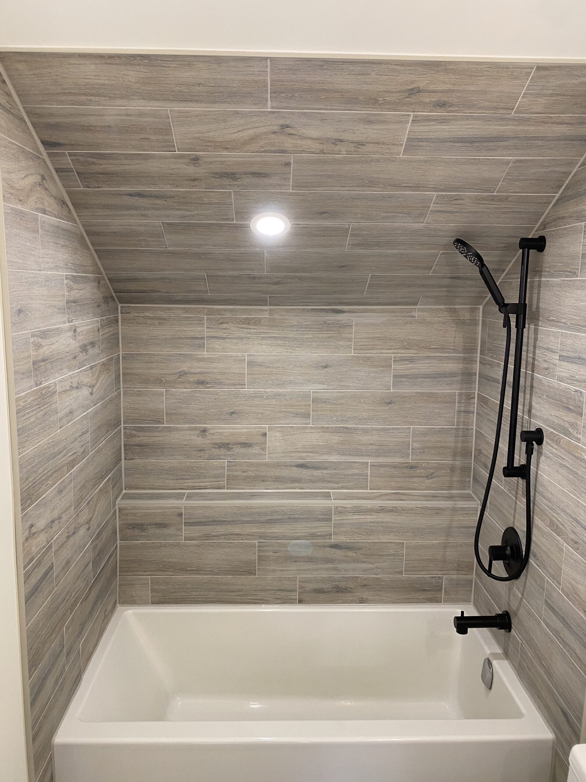 Bathroom tub and shower with wood-style tiling all around in a nook in the bathroom.