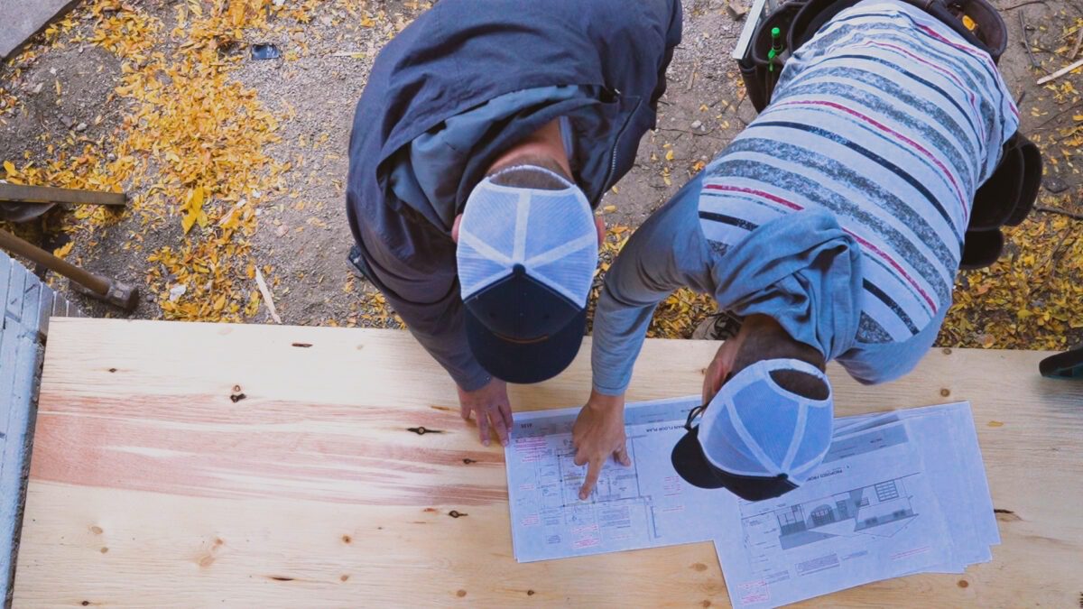 Keith Groen reviews structural drawings with a carpenter on a jobsite outdoors.