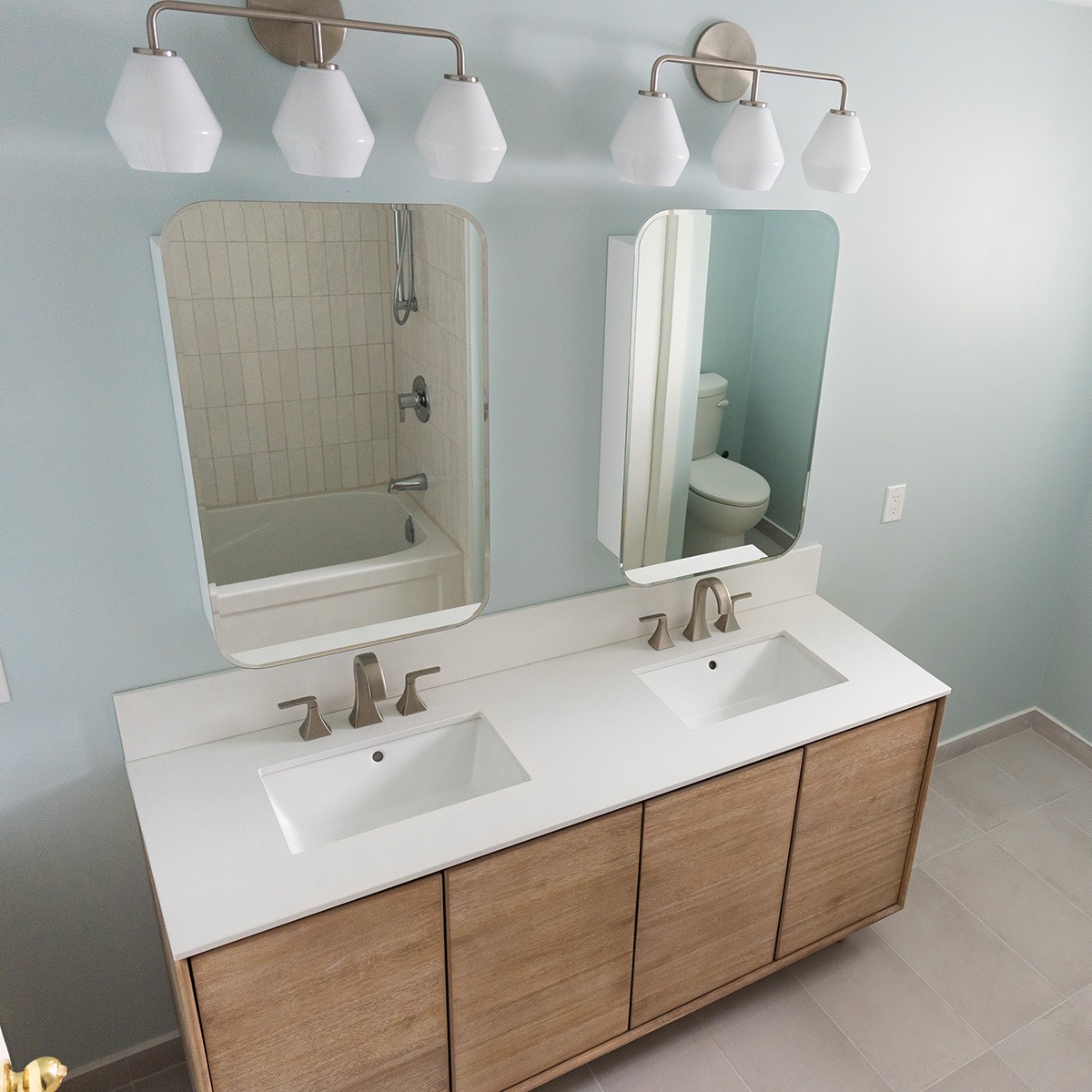 Looking down at a double vanity in a newly renovated bathroom with two ornate light fixtures and two identical mirrors over the vanity.