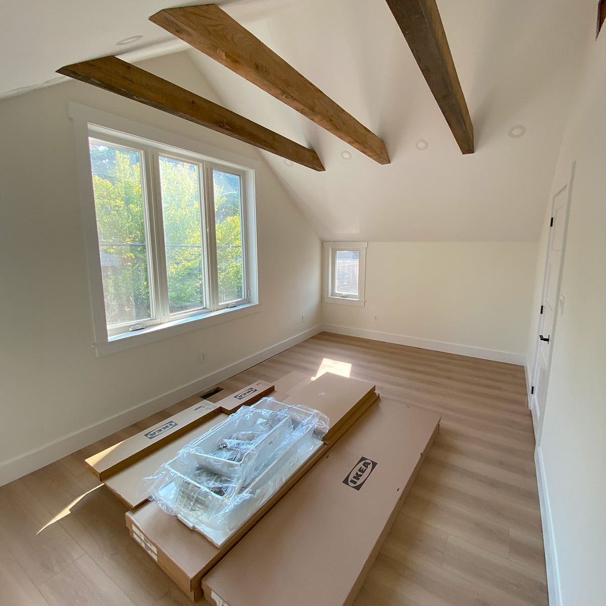 A bright, open bedroom with exposed wood beams in the ceiling.